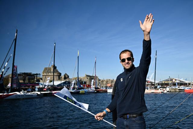 British sailor Sam Goodchild waves to the public aboard his "Macif Sante Prevoyance" IMOCA Class as he prepares to pass through the Naye lock of Saint-Malo's harbour, to moor off the coast of Saint-Malo northwestern France on October 31, 2026 on the eve of the start of the Route du Rhum solo sailing race from Saint-Malo, to Pointe-a-Pitre in the French overseas island of Guadeloupe. (Photo by Loic VENANCE / AFP)