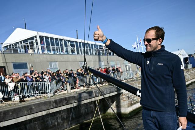 British sailor Sam Goodchild waves to the public aboard his "Macif Sante Prevoyance" IMOCA Class as he prepares to pass through the Naye lock of Saint-Malo's harbour, to moor off the coast of Saint-Malo northwestern France on October 31, 2026 on the eve of the start of the Route du Rhum solo sailing race from Saint-Malo, to Pointe-a-Pitre in the French overseas island of Guadeloupe. (Photo by Loic VENANCE / AFP)
