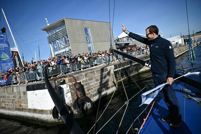 British sailor Sam Goodchild waves to the public aboard his "Macif Sante Prevoyance" IMOCA Class as he prepares to pass through the Naye lock of Saint-Malo's harbour, to moor off the coast of Saint-Malo northwestern France on October 31, 2026 on the eve of the start of the Route du Rhum solo sailing race from Saint-Malo, to Pointe-a-Pitre in the French overseas island of Guadeloupe. (Photo by Loic VENANCE / AFP)