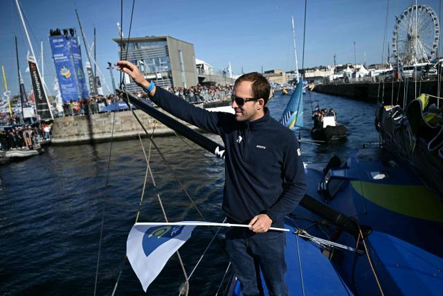 British sailor Sam Goodchild waves to the public aboard his "Macif Sante Prevoyance" IMOCA Class as he prepares to pass through the Naye lock of Saint-Malo's harbour, to moor off the coast of Saint-Malo northwestern France on October 31, 2026 on the eve of the start of the Route du Rhum solo sailing race from Saint-Malo, to Pointe-a-Pitre in the French overseas island of Guadeloupe. (Photo by Loic VENANCE / AFP)