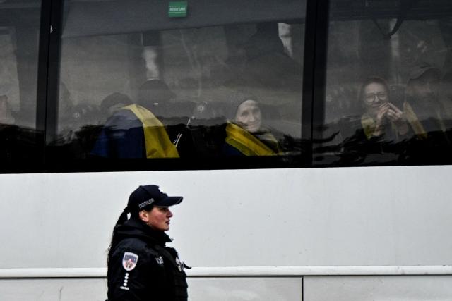 Residents evacuated from the Russian-controlled city of Oleshky during a humanitarian mission react next to a window sitting in a bus as a police officer stands, upon arriving at an undisclosed location in Ukraine on October 31, 2026, amid the Russian invasion of Ukraine. Residents of the Russian-controlled city of Oleshky, ravaged by years of war, arrived in Ukraine on October 31, 2026 after being evacuated via Belarus during a rare truce. (Photo by Genya Savilov / AFP)