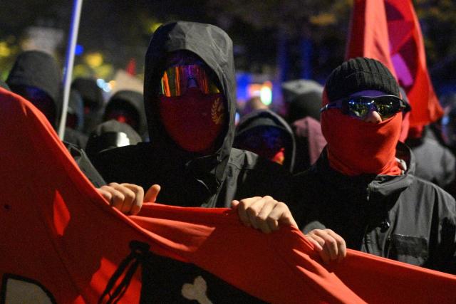 Masked protesters hold a banner as they march during a demonstration in Berlin on October 31, 2026. The German demonstrations have been inspired by similar movements across Europe, including in France and Italy, which have seen young protesters voice anger at political elites whom they accuse of ignoring their concerns. (Photo by RALF HIRSCHBERGER / AFP)