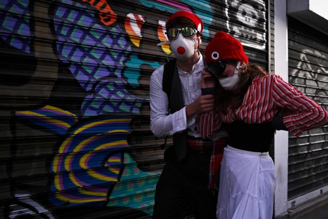 A protester accompanies another dressed in French symbol Marianne as she reacts from tear gas during nationwide demonstrations over the rising cost of living and inequality organised by Yellow Vest movement, labour unions and high school and university students, in Paris on October 31, 2026. "Exceptional" security deployment with 70,000 police officers and gendarmes mobilized and an alarmist tone: for Act III of the protests against the high cost of living, right in the middle of Halloween festivities, the authorities fear a repeat of the October 17 nightmare. France has been rocked by widespread anger over the rising cost of living and inequality. (Photo by JULIEN DE ROSA / AFP)