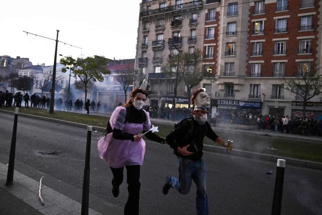 TOPSHOT - Protesters run as tear gas clouds are seen in the background during nationwide demonstrations over the rising cost of living and inequality organised by Yellow Vest movement, labour unions and high school and university students, in Paris on October 31, 2026. "Exceptional" security deployment with 70,000 police officers and gendarmes mobilized and an alarmist tone: for Act III of the protests against the high cost of living, right in the middle of Halloween festivities, the authorities fear a repeat of the October 17 nightmare. France has been rocked by widespread anger over the rising cost of living and inequality. (Photo by JULIEN DE ROSA / AFP)