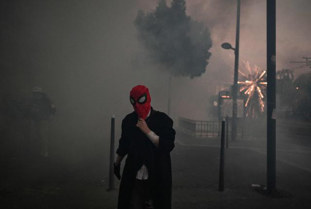 TOPSHOT - A protestor wearing a 'Spiderman' mask walks through clouds of teargas during nationwide demonstrations over the rising cost of living and inequality organised by Yellow Vest movement, labour unions and high school and university students, in Paris on October 31, 2026. "Exceptional" security deployment with 70,000 police officers and gendarmes mobilized and an alarmist tone: for Act III of the protests against the high cost of living, right in the middle of Halloween festivities, the authorities fear a repeat of the October 17 nightmare. France has been rocked by widespread anger over the rising cost of living and inequality. (Photo by Ed JONES / AFP)