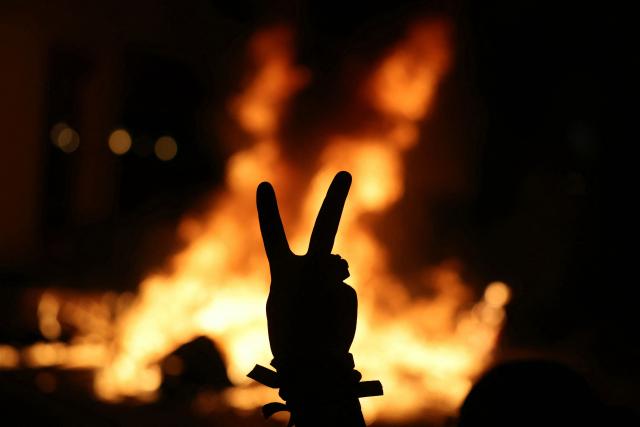 A protester flashes a "V" sign with a street fire in the background during nationwide demonstrations over the rising cost of living and inequality organised by Yellow Vest movement, labour unions and high school and university students, in Nantes, western France on October 31, 2026. "Exceptional" security deployment with 70,000 police officers and gendarmes mobilized and an alarmist tone: for Act III of the protests against the high cost of living, right in the middle of Halloween festivities, the authorities fear a repeat of the October 17 nightmare. France has been rocked by widespread anger over the rising cost of living and inequality. (Photo by ALAIN JOCARD / AFP)