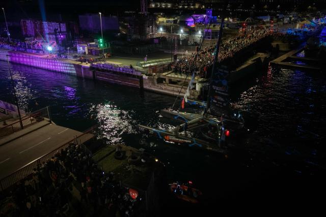 This aerial photograph shows "Solidaires en Peloton by Delanchy" Ocean Fifty Class French sailor Thibaut Vauchel-Camus sailing and leaving at night the harbour of Saint-Malo, western France, on October 31, 2026, ahead of the start of the 13th Route du Rhum - Destination Guadeloupe solo sailing race from Saint-Malo, western France to Pointe-a-Pitre in the French overseas island of Guadeloupe. (Photo by LOU BENOIST / AFP)