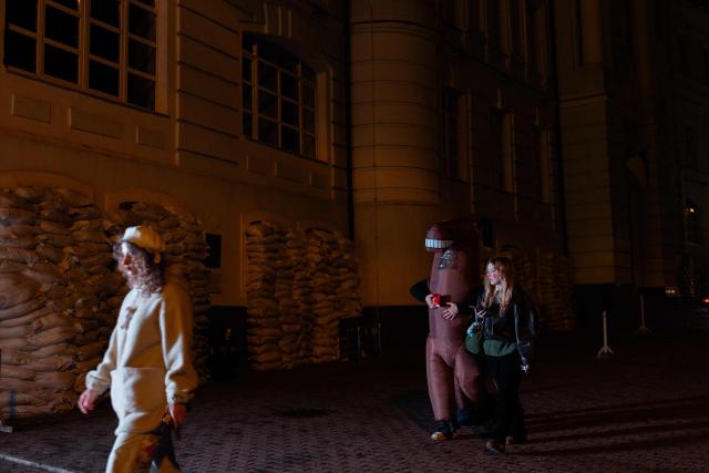 People dressed in Halloween costumes walk past window-protecting sandbags during a partial power outages following Russian attacks in Kyiv on October 31, 2026, amid the Russian invasion of Ukraine. (Photo by Tetiana DZHAFAROVA / AFP)