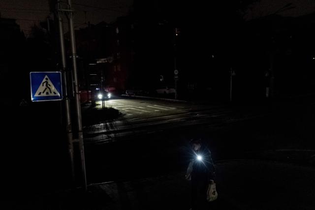 A man with uses a flashlight as he walks down a dark street during partial power outages following Russian attacks in Kyiv on October 31, 2026, amid the Russian invasion of Ukraine. (Photo by Tetiana DZHAFAROVA / AFP)