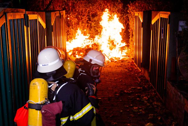 31 October 2024, Hamburg: Firefighters stand by a burning garbage container on Halloween night. Photo: Daniel Bockwoldt/dpa