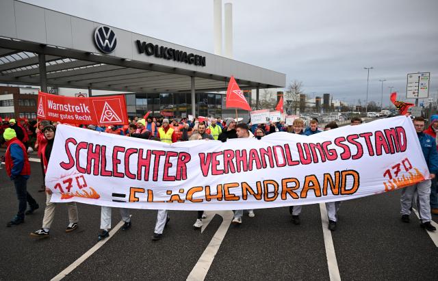 02 December 2024, Saxony, Zwickau: Volkswagen employees go on a warning strike in front of the Zwickau plant behind a banner with the slogan "Bad negotiations = wildfire". Europe's largest car manufacturer, Volkswagen, is launching nationwide warning strikes on 02 December. IG Metall intends to bring production to a temporary standstill with temporary work stoppages at all German sites. The so-called peace obligation expired at the weekend. Photo: Hendrik Schmidt/dpa