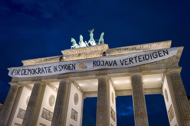 FILED - 16 December 2024, Berlin: Pro-Kurdish activists unfurl a banner reading "For democracy in Syria - Defend Rojava" at the Brandenburg Gate, as a symbol of solidarity with the Kurdish regions in Syria. Photo: Michael Ukas/dpa