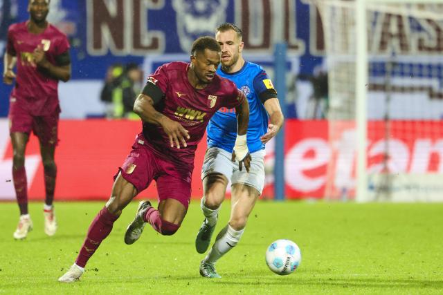 21 December 2024, Schleswig-Holstein, Kiel: Augsburg's Samuel Essende (L) and Kiel's Marco Komenda battle for the ball during the German Bundesliga soccer match between Holstein Kiel and FC Augsburg at Holstein Stadium. Photo: Frank Molter/dpa - IMPORTANT NOTICE: DFL and DFB regulations prohibit any use of photographs as image sequences and/or quasi-video.