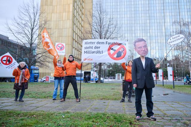 27 January 2025, Berlin: An Attac activist is seen wearing mask depicting businessman and political figure Elon Musk, while others hold a banner reading "Behind fascism is the billionaire!", during a demonstration in front of the Axel Springer skyscraper in conjunction with an economic summit by the German newspaper "Die Welt". Photo: Annette Riedl/dpa