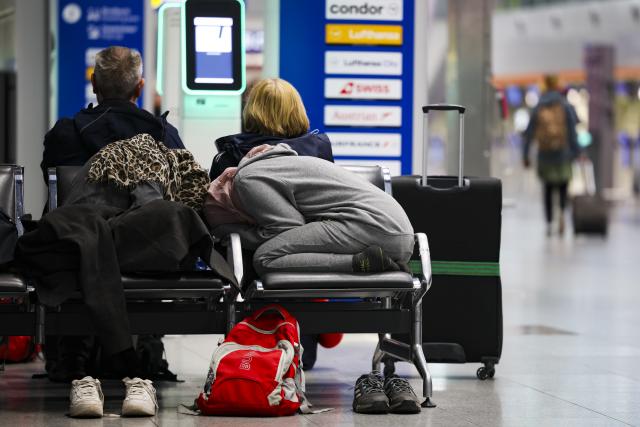 10 March 2025, North Rhine-Westphalia, Duesseldorf: Two travellers rest on a bench in the departure terminal at Duesseldorf Airport, their heads covered with scarves and their shoes placed on the floor. The Verdi union has called for a 24-hour warning strike by public service and ground handling workers at eleven airports on Monday. Photo: Christoph Reichwein/dpa