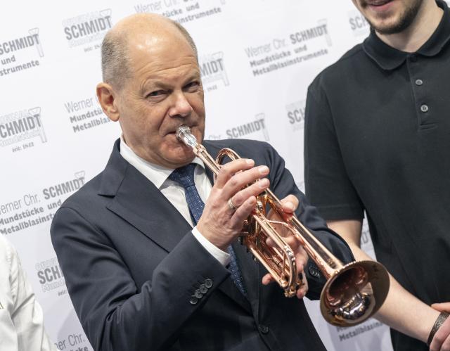 14 March 2025, Bavaria, Munich: Germany's Chancellor Olaf Scholz plays a trumpet made of pure copper during a tour of the International Crafts Fair. Earlier, he attended the meeting of the presidents of Germany's four leading industry associations. Photo: Peter Kneffel/dpa