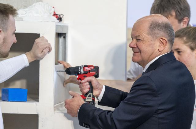 14 March 2025, Bavaria, Munich: Germany's Chancellor Olaf Scholz uses a cordless screwdriver to tighten a plasterboard during a tour of the International Crafts Fair. Earlier, he attended the meeting of the presidents of Germany's four leading industry associations. Photo: Peter Kneffel/dpa