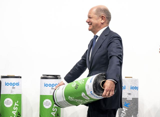 14 March 2025, Bavaria, Munich: Germany's Chancellor Olaf Scholz holds a bitumen waterproofing membrane in his hands during a tour of the International Crafts Fair. Earlier, he attended the meeting of the presidents of Germany's four leading industry associations. Photo: Peter Kneffel/dpa