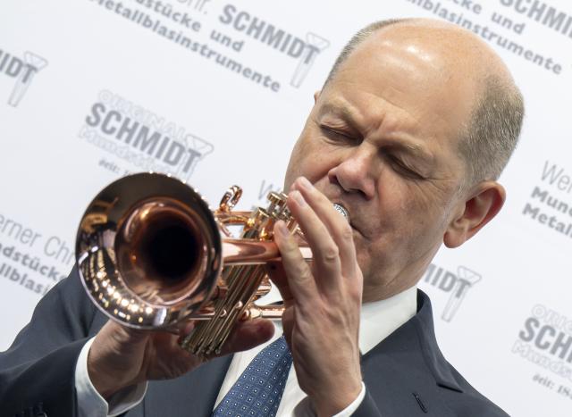 14 March 2025, Bavaria, Munich: Germany's Chancellor Olaf Scholz plays a trumpet made of pure copper during a tour of the International Crafts Fair. Earlier, he attended the meeting of the presidents of Germany's four leading industry associations. Photo: Peter Kneffel/dpa