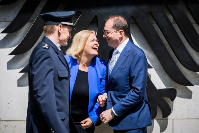 07 May 2025, Berlin: (R-L) Alexander Dobrindt, new German Minister of the Interior and Home Affairs, and Nancy Faeser, former Minister of the Interior and Home Affairs, speak next to a federal police officer at the protocol entrance of the Federal Ministry of the Interior and Home Affairs during a photo session marking the handover of official duties. Photo: Christoph Soeder/dpa