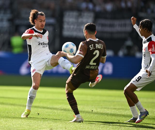 11 May 2025, Hesse, Frankfurt/Main: Frankfurt's Arthur Theate (L) and Jean-Matteo Bahoya (R) battle for the ball with St. Pauli's Manolis Saliakas  during the German Bundesliga soccer match between Eintracht Frankfurt and FC St. Pauli at Deutsche Bank Park. Photo: Arne Dedert/dpa - WICHTIGER HINWEIS: Gemäß den Vorgaben der DFL Deutsche Fußball Liga bzw. des DFB Deutscher Fußball-Bund ist es untersagt, in dem Stadion und/oder vom Spiel angefertigte Fotoaufnahmen in Form von Sequenzbildern und/oder videoähnlichen Fotostrecken zu verwerten bzw. verwerten zu lassen.