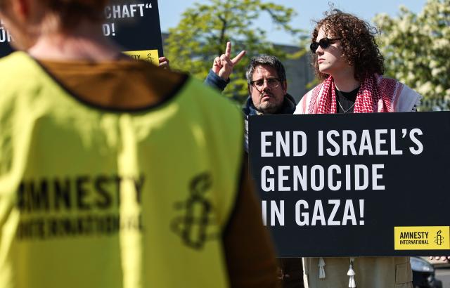12 May 2025, Berlin: A participant in an Amnesty International protest against the Israeli war in the Gaza Strip holds a sign reading "End Israel's Genocide in Gaza" in front of the Federal Chancellery. The Israeli President visits Germany to mark the establishment of diplomatic relations between the Federal Republic of Germany and Israel 60 years ago. Photo: Hannes P. Albert/dpa