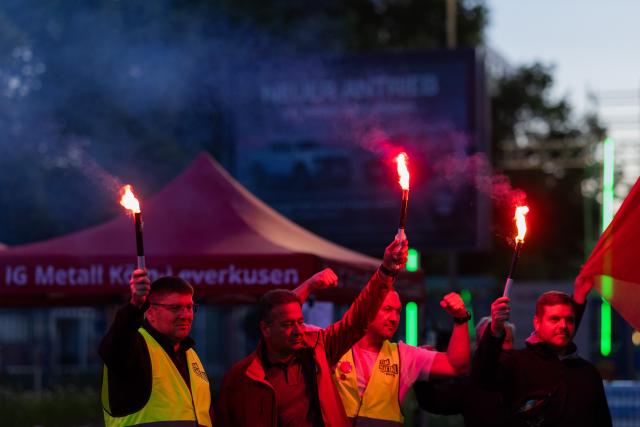14 May 2025, North Rhine-Westphalia, Cologne: Employees with burning torches stand in front of the Ford plants in Cologne during the first strike. A strike is taking place for the first time at the Ford plants in Cologne. The protest action against planned job cuts at the site with 11,500 employees is to begin on Wednesday morning and last until the end of the night shift on Thursday morning, according to IG Metall. Photo: Rolf Vennenbernd/dpa