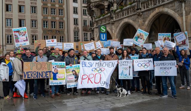 28 May 2025, Bavaria, Munich: Several people take part in a demonstration on Munich's Marienplatz in support of Munich's planned Olympic bid and hold placards. A banner in the middle reads "BLSV Munich - PROlympia". The demonstration was organized by the Bavarian State Sports Association and Allianz Munich. Photo: Leonie Asendorpf/dpa