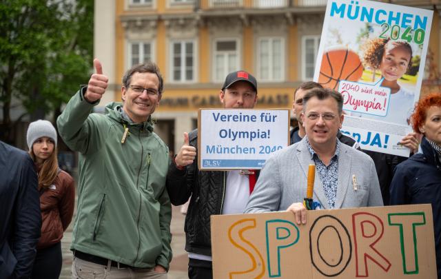 28 May 2025, Bavaria, Munich: Several people take part in a demonstration on Marienplatz in support of Munich's planned Olympic bid, holding placards including the slogan "Clubs for the Olympics - Munich 2040". The demonstration was organized by the Bavarian State Sports Association and Allianz Munich. Photo: Leonie Asendorpf/dpa