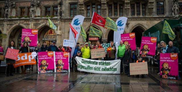 28 May 2025, Bavaria, Munich: Several people take part in a demonstration on Munich's Marienplatz against Munich's planned Olympic bid. The demonstrators hold a banner with the inscription "Strengthen democracy - do not disregard the will of the citizens". The motto of the demonstration is: "nOlympia: Munich must not burn money for the IOC and destroy nature!". Photo: Leonie Asendorpf/dpa