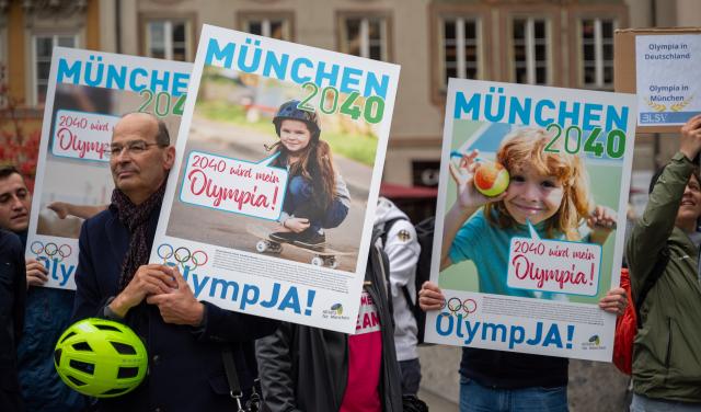 28 May 2025, Bavaria, Munich: Several people take part in a demonstration on Marienplatz in support of Munich's planned Olympic bid and hold placards, including one reading "Munich 2040 - 2040 will be my Olympia - OlympJa". The demonstration was organized by the Bavarian State Sports Association and Allianz Munich. Photo: Leonie Asendorpf/dpa