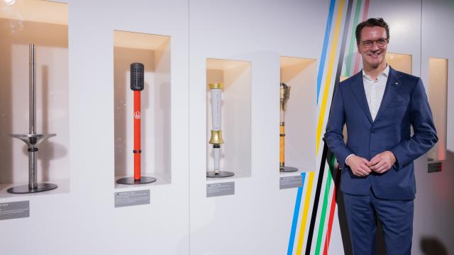 28 May 2025, North Rhine-Westphalia, Cologne: Hendrik Wuest, Minister President of North Rhine-Westphalia, stands next to torches from past Olympic Games such as Munich 1972 (l) at the presentation of the concept of an Olympic bid with the Rhine-Ruhr region for the Olympic Games. Photo: Rolf Vennenbernd/dpa