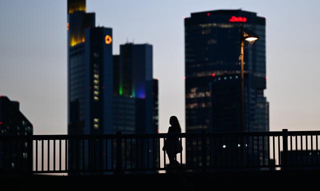 01 July 2025, Hesse, Frankfurt/Main: A woman walks across the Floesserbruecke bridge at sunset on a warm tropical evening, with skyscrapers silhouetted in the background. Photo: Arne Dedert/dpa