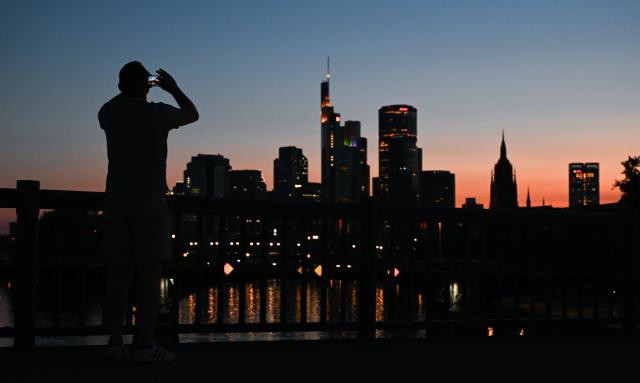 01 July 2025, Hesse, Frankfurt/Main: A man photographs the skyline at sunset on a warm tropical evening. Photo: Arne Dedert/dpa