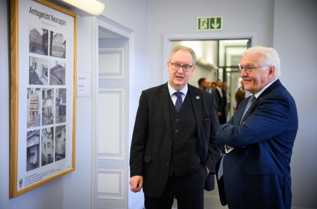 03 July 2025, Brandenburg, Neuruppin: German President Frank-Walter Steinmeier visits the Neuruppin district court and is shown historical photos by the court's director Frank Juettner. German President Steinmeier has moved his official residence to Neuruppin for three days as part of the This is the 16th time that "Local Time Germany" has taken place, during which the German head of state spends three days in a small town away from the big cities to gather information and talk to citizens. Photo: Bernd von Jutrczenka/dpa