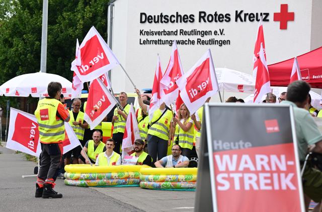 03 July 2025, Baden-Württemberg, Reutlingen: Employees of the German Red Cross (DRK) stand in front of a rescue station during a warning strike with union flags at a rally. The union is calling for work stoppages in the ongoing nationwide collective bargaining round with the German Red Cross. Photo: Bernd Weißbrod/dpa