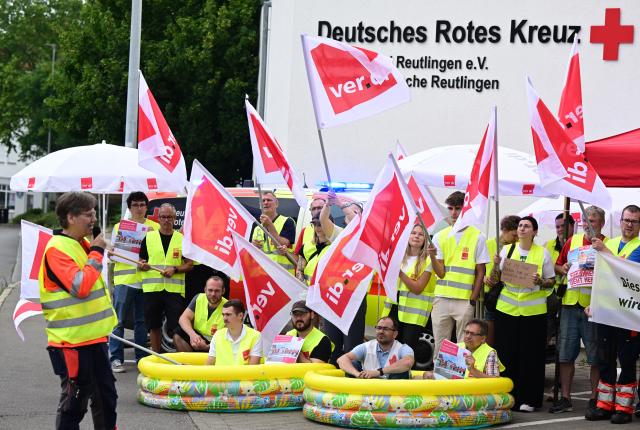 03 July 2025, Baden-Württemberg, Reutlingen: Employees of the German Red Cross (DRK) stand and sit in paddling pools during a warning strike with union flags in front of a rescue station. The union is calling for work stoppages in the ongoing nationwide collective bargaining round with the German Red Cross. Photo: Bernd Weißbrod/dpa