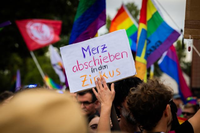 05 July 2025, Brandenburg, Falkensee: A participant holds a sign at reading "Deport Merz to the circus" in German, during the Christopher Street Day (CSD) procession through Falkensee. Photo: Christoph Soeder/dpa