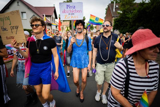 05 July 2025, Brandenburg, Falkensee: A participant holds a sign at reading "Deport Merz to the circus" in German, during the Christopher Street Day (CSD) procession through Falkensee. Photo: Christoph Soeder/dpa