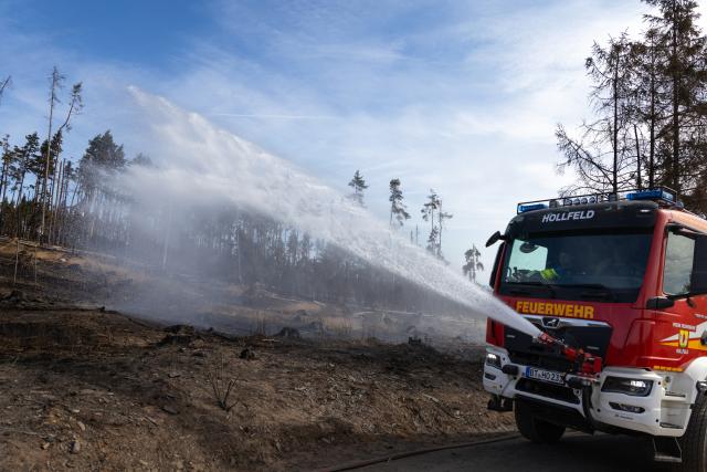 06 July 2025, Thuringia, Reichmannsdorf: A fire engine from Bayreuth sprays extinguishing water onto hidden pockets of embers at the forest fire on the Saalfelder Hoehe. Photo: Michael Reichel/dpa