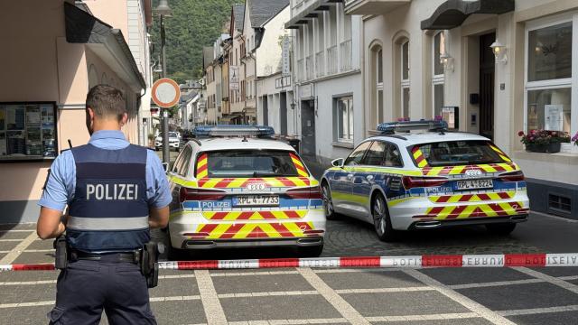 14 August 2025, Rheinland-Pfalz, Bad Bertrich: Police cars stand behind a cordon in a pedestrian zone, where a resident is said to have attacked police officers during a search of a building in Bad Bertrich. Photo: Kevin Schössler/dpa