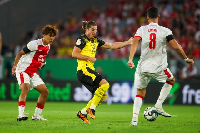 18 August 2025, North Rhine-Westphalia, Essen: Borussia Dortmund's Marcel Sabitzer (C) battles for the ball with Essen's Kaito Mizuta (L) and Klaus Gjasula during the German DFB Cup 1st round soccer match between Rot-Weiss Essen and Borussia Dortmund at Stadion an der Hafenstrasse. Photo: Christoph Reichwein/dpa - WICHTIGER HINWEIS: Gemäß den Vorgaben der DFL Deutsche Fußball Liga bzw. des DFB Deutscher Fußball-Bund ist es untersagt, in dem Stadion und/oder vom Spiel angefertigte Fotoaufnahmen in Form von Sequenzbildern und/oder videoähnlichen Fotostrecken zu verwerten bzw. verwerten zu lassen.