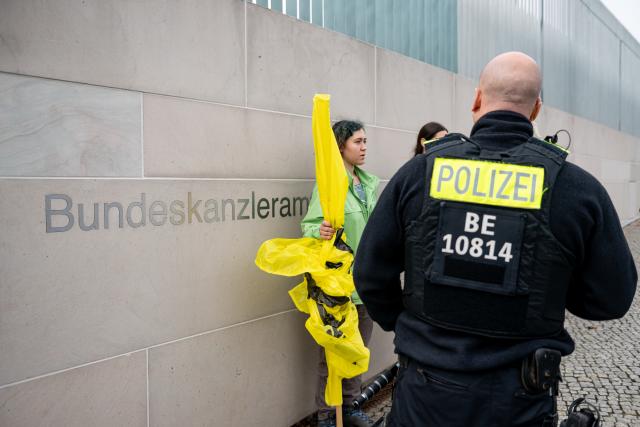 09 October 2025, Berlin: Greenpeace activists confront a police officer in front of the Chancellery.  Representatives from politics, manufacturers and suppliers, associations and trade unions as well as the federal states with the car industry come together for a so-called car summit Photo: Fabian Sommer/dpa