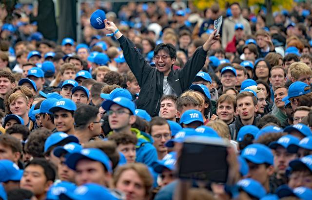 13 October 2025, Bavaria, Garching: Students in blue TUM caps stand in front of the stage at the start of the semester at the TUM campus. Photo: Malin Wunderlich/dpa