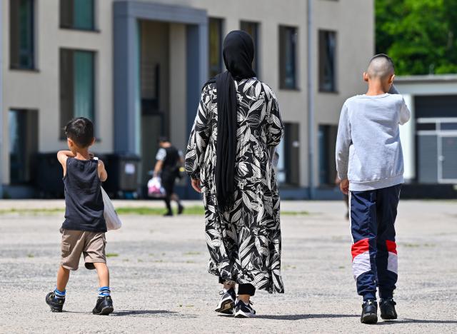 FILED - 18 June 2024, Brandenburg, Eisenhuettenstadt: A migrant woman and her two children walk through the grounds of the Central Reception Center for Asylum Seekers (ZABH) in Brandenburg. Almost two-thirds of refugees in Germany are at risk of poverty, a leading economic institute has found. Photo: Patrick Pleul/dpa