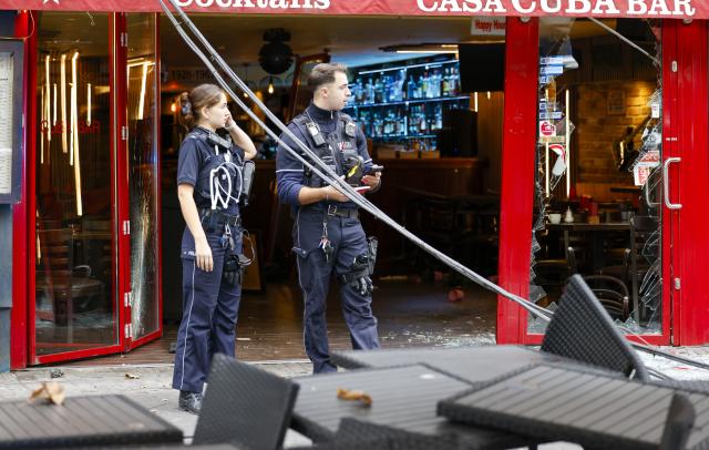 17 October 2025, North Rhine-Westphalia, Cologne: Police officers stand on the sidewalk in front of the facade of a partially destroyed bar. A 73-year-old driver drove through a glass frontage into a bar in Cologne city center. Fortunately, the bar was empty at the time, said a police spokesman. Photo: Thomas Banneyer/dpa