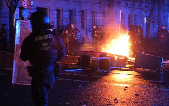 17 October 2025, Saxony, Leipzig: Police officers stand in front of burning objects on Eisenbahnstrasse as Left-wing activists stage a spontaneous demonstration to protest against the eviction of squats. Photo: Sebastian Willnow/dpa
