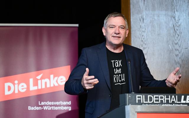 18 October 2025, Baden-Wuerttemberg, Leinfelden-Echterdingen: Jan van Aken, party chairman of Die Linke, speaks at the Baden-Wuerttemberg state party conference and casts a shadow over the party's logo. Photo: Bernd Weißbrod/dpa