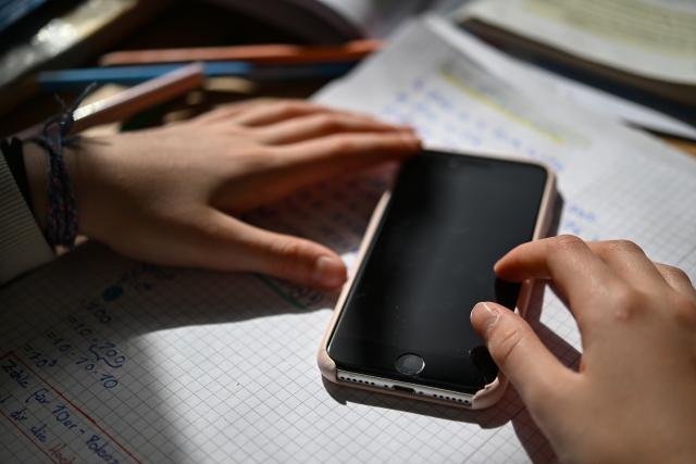 FILED - 08 April 2025, Baden-Wuerttemberg, Stuttgart: A schoolchild sits at a desk with school materials and holds a smartphone in his hands. Photo: Marijan Murat/dpa