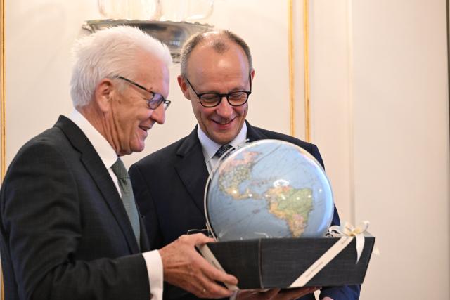 21 October 2025, Baden-Württemberg, Stuttgart: Winfried Kretschmann (L), Minister President of Baden-Wuerttemberg, presents a gift to German Chancellor Friedrich Merz at Villa Reitzenstein. Chancellor Merz is on his inaugural visit to Baden-Wuerttemberg. Photo: Marijan Murat/dpa